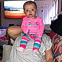 baby, child, person, indoor, colorful_clothing, pink_shirt, striped_pants, socks, adult, shoulders, living_room, television, quilt, couch, curious, seated, portrait, cute, face, head