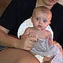 Gracie is registered to the contest to win money with this photo: baby, woman, person, indoor, couch, clothing, earbuds, holding, striped_cloth, diaper, seated, skin, face, legs, casual, young_adult, curious, expression, home, relaxed