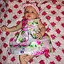 Gracie is registered to the contest to win money with this photo: baby, infant, child, floral_dress, headband, pink, quilt, pattern, red_flowers, lying_down, barefoot, cute, portrait, indoors, skin, face, arms, legs, expression, background