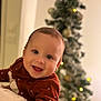 baby, child, smiling, face, red_sweater, white_dots, christmas_tree, ornaments, lights, holiday, festive, indoors, portrait, happy, infant, cozy, blurred_background, warm, cute, person
