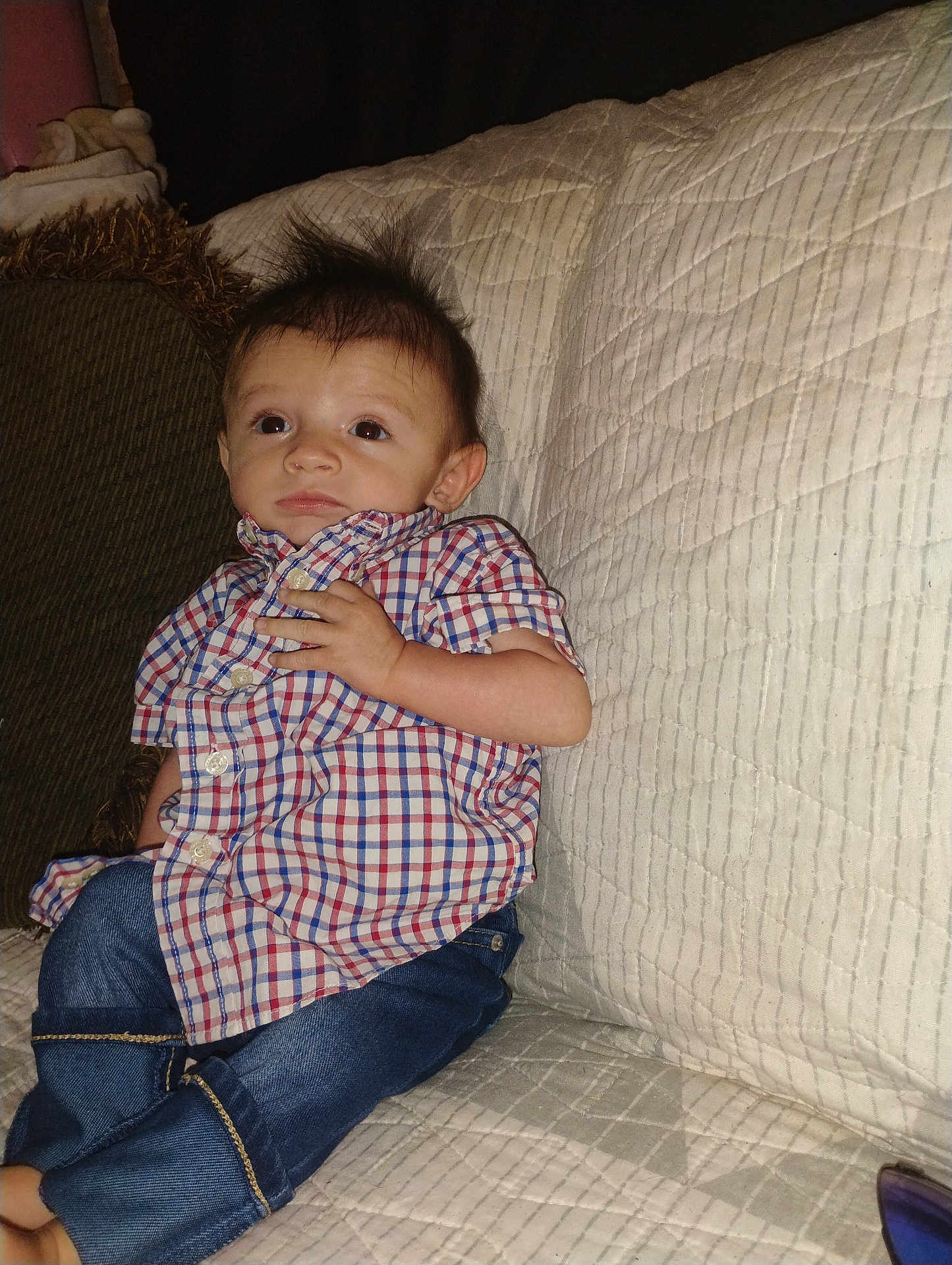 Christian is registered to the contest to win money with this photo: child, baby, infant, plaid_shirt, jeans, couch, quilt, pillow, hair, wide_eyes, sitting, indoor, portrait, hand, button_down, flash_photography, cute, expression, furniture, casual_clothing