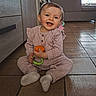 baby, child, smiling, toy, pink_outfit, socks, floor, tile_floor, indoor, happy, cute, sitting, person, face, home, furniture, cabinet, playful, infant, headband