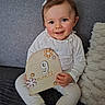 Loélye participe au concours pour gagner de l'argent avec cette photo : baby, child, smile, couch, white_clothing, wooden_sign, flowers, sitting, portrait, indoor, cute, happy, face, hair_clip, plush_pillow, cozy, infant, hands, tongue, skin