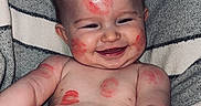 Oakley is registered to the contest to win money with this photo: baby, infant, smiling, face, red_marks, lipstick, skin, blanket, striped_blanket, happy, cheeks, arms, chest, sitting, cute, closeup, portrait, indoors, playful, child