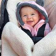Oakley joined the competition — help win amazing prizes! baby, smiling, hood, pink_clothing, blanket, stroller, fuzzy, face, child, infant, happy, cute, warm, cozy, soft_texture, seated, indoor, clothing, baby_carrier, portrait