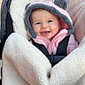 baby, smiling, hood, pink_clothing, blanket, stroller, fuzzy, face, child, infant, happy, cute, warm, cozy, soft_texture, seated, indoor, clothing, baby_carrier, portrait