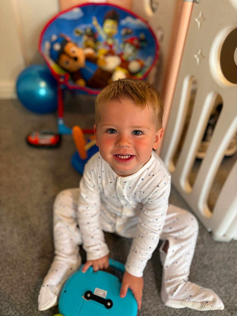 Leo joined the competition — help win amazing prizes! toddler, child, pajamas, toy, carpet, indoor, smiling, sitting, floor, playroom, childrens_chair, cartoon_characters, blue, white, happy, cute, hair, face, hands, feet