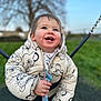 child, toddler, smiling, jacket, hooded_clothing, outdoor, swing, playground, happy, blue_sky, tree, grass, winter_clothing, cute, face, person, young_child, daylight, holding, fun