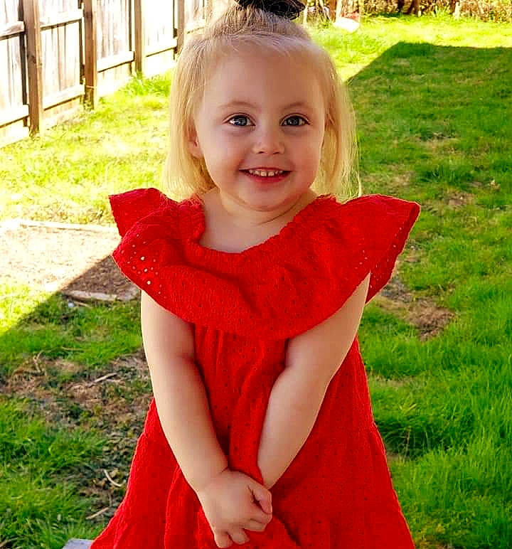 Hadleigh is registered to the contest to win money with this photo: blond, child, child_model, clothing, dress, grass, joy, pattern, person, red, shoulder, smile, textile, toddler