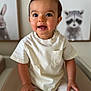 toddler, child, smiling, indoor, portrait, white_tshirt, beige_pants, hands, face, eyes, hair, furniture, wall_art, animal_painting, raccoon, rabbit, cute, young_child, seated, cozy