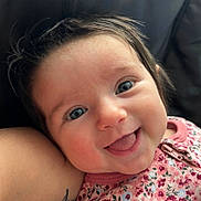 Eliana is registered to the contest to win money with this photo: baby, child, face, smile, tongue, blue_eyes, floral_clothing, infant, cute, closeup, skin, hair, cheeks, person, tattoo, arm, happy, expression, indoors, portrait