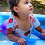 child, toddler, curly_hair, inflatable_pool, water, water_toy, blue_shovel, ball, swimsuit, strawberry_print, cute, outdoor, summer, portrait, looking_up, playtime, hand, skin, grass, tree