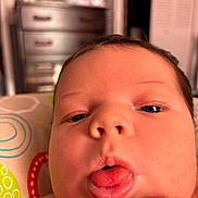 Skyler joined the competition — help win amazing prizes! baby, close_up, tongue, face, infant, skin, expression, indoors, blurred_background, furniture, drawer, patterned_pillow, cute, child, person, newborn, head, mouth, hand, young