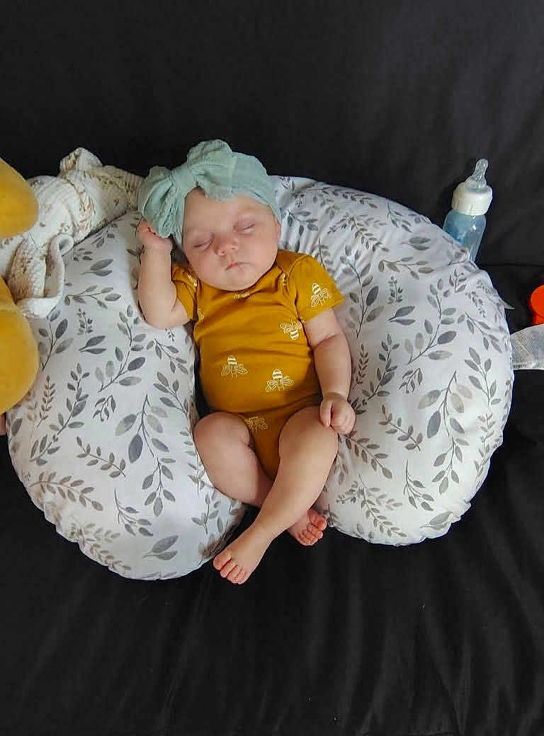 Hazel joined the competition — help win amazing prizes! baby, sleeping, onesie, headband, nursing_pillow, couch, bottle, infant, peaceful, resting, yellow_clothing, patterned_pillow, child, cute, soft, indoor, relaxed, small, adorable, peaceful_sleep