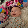 baby, smiling, blanket, bed, floral_clothing, infant, happy, cute, lying_down, indoors, soft_texture, polka_dot, child, one_piece, portrait, face, cozy, colorful, young, comfort