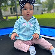 Delilah Rain joined the competition — help win amazing prizes! baby, child, girl, headband, bow, blue_hoodie, pink_pants, socks, trampoline, outdoor, fence, grass, curious, portrait, sitting, cute, infant, young_child, daylight, play