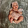 baby, infant, child, pink_dress, headband, lace, blanket, soft_texture, card, barefoot, lying_down, curious, cute, indoor, portrait, young_child, skin, hands, feet, expression