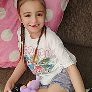 Gabriel joined the competition — help win amazing prizes! child, girl, braids, smile, couch, remote_control, plush_toy, white_tshirt, denim_shorts, black_bows, polka_dot_blanket, indoor, casual_clothing, happy, seated, home, furniture, person, cute, relaxed
