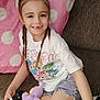 child, girl, braids, smile, couch, remote_control, plush_toy, white_tshirt, denim_shorts, black_bows, polka_dot_blanket, indoor, casual_clothing, happy, seated, home, furniture, person, cute, relaxed