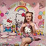 child, birthday_party, hello_kitty, balloons, party_decorations, smiling, girl, table, piñata, colorful, pink, cake, plates, gifts, shorts, tshirt, long_hair, indoors, celebration, footwear