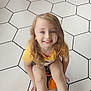 Adam Jr. is registered to the contest to win money with this photo: child, smiling, sitting, soccer_ball, yellow_shirt, long_hair, blue_eyes, indoor, floor_tiles, white_floor, black_grout, green_shoes, cartoon_shoes, happy, playful, young_child, person, floor, casual_clothing, bright_lighting