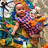 activity_gym, baby, carpet, checkered_clothing, child, colorful, face, happy, indoor, infant, lying_down, nursery, overhead_view, play_mat, playtime, portrait, romper, smiling, stuffed_animal, toys