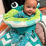 activity_seat, baby, baby_walker, bedroom, cartoon_eyes, child, colorful, cozy, cushion, face, floral_outfit, happy, indoors, infant, photography, playful, portrait, seated, smiling, toy