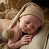 baby, sleeping, hat, pom_pom, pillow, blanket, soft_texture, newborn, peaceful, cozy, infant, close_up, portrait, cute, resting, indoors, warm_colors, skin, hands, face