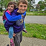 child, children, playful, piggyback, outdoor, sidewalk, grass, trees, cloudy_sky, casual_clothing, sneakers, happy, funny_face, siblings, nature, young, smiling, joy, park, portrait