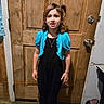 black_outfit, blue_shrug, bows, casual, child, door_lock, floor, girl, hair_tied, indoor, jewelry, leopard_print_shoe, necklace, person, rustic, shoes, smiling, standing, wood, wooden_door