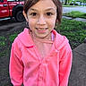 casual_wear, child, curious, daylight, earrings, face, girl, greenery, happy, hoodie, outdoor, person, pink_clothing, portrait, sidewalk, smile, tree, truck, vehicle, young