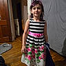 casual_clothing, child, colorful, curtain, door, dress, fabric, flooring, floral_pattern, footwear, holding, indoor, person, purple_hair, room, standing, striped_clothing, wall, wooden_floor, young
