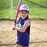 activity, athlete, baseball, bat, cap, child, determined, fence, field, girl, grass, knee_socks, outdoor, ready, sand, sport, sportswear, sunny, team, youth