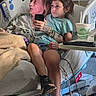 Davina is registered to the contest to win money with this photo: adult, bedside_table, blanket, charger, child, drink_cup, family, girl, hospital, hospital_bed, indoors, medical_equipment, monitor, patient, phone, portrait, shoes, shorts, sitting, striped_shirt