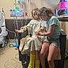 birthday_bag, caregiving, chair, child, colorful_socks, denim_shorts, family, girl, heart_monitor, hospital, hospital_bed, infusion_pump, iv_bag, iv_pole, medical_equipment, medical_room, patient, sitting, striped_shirt, water_bottle