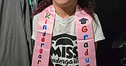 Davina is registered to the contest to win money with this photo: child, girl, kindergarten, graduate, sash, tshirt, indoor, person, smile, hair, curtain, mop, floor, portrait, celebration, clothing, young, standing, achievement, face