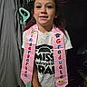 child, girl, kindergarten, graduate, sash, tshirt, indoor, person, smile, hair, curtain, mop, floor, portrait, celebration, clothing, young, standing, achievement, face