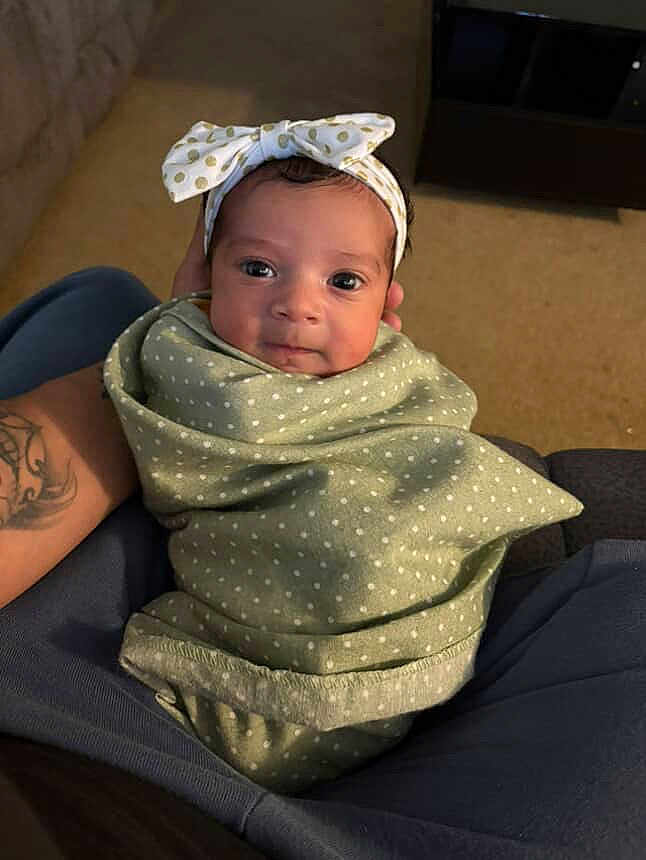 Novalyn is registered to the contest to win money with this photo: baby, infant, blanket, headband, polka_dot, tattoo, arm, carpet, living_room, person, cute, smiling, wrapped, seated, indoor, young_child, comfort, soft, portrait, cozy