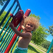 Tydus joined the competition — help win amazing prizes! child, toddler, curly_hair, playground, outdoor, sunny, blue_sky, red_panel, green_shorts, summer, park, metal_bars, happy, play, nature, grass, tree, daytime, smile, person