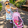 Ocean Rae is registered to the contest to win money with this photo: toddler, child, sunglasses, headband, dress, toy_stroller, doll, toy_phone, pathway, garden, flowers, bench, sunlight, shoes, outdoor, summer, play, cute, park, greenery