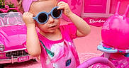 Ocean Rae is registered to the contest to win money with this photo: child, toddler, sunglasses, pink, dress, unicorn, toy_car, barbie, headband, playroom, indoor, decor, carpet, plant, door, flowers, toy, fun, cute, portrait