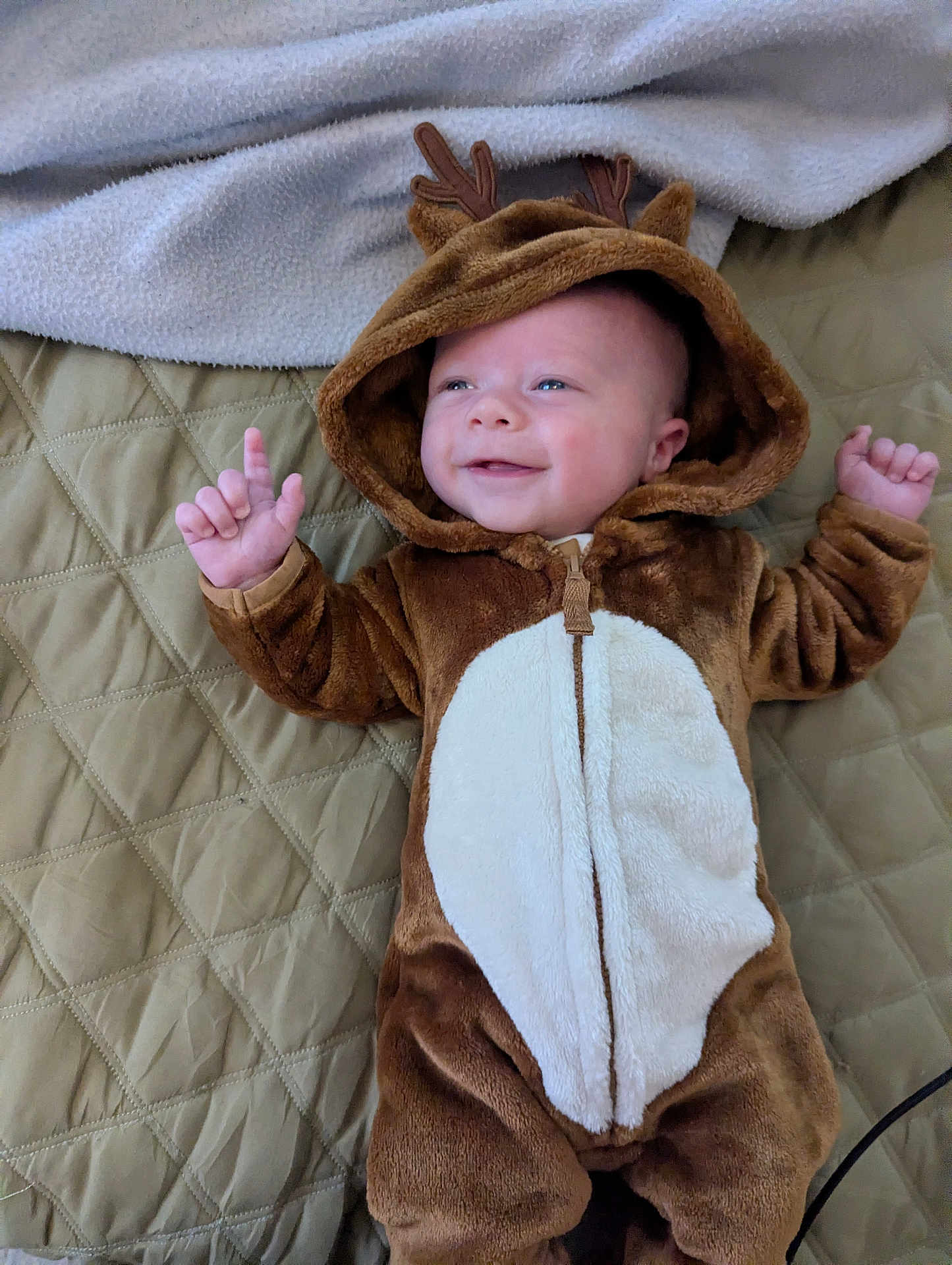 Ashton is registered to the contest to win money with this photo: baby, infant, child, smiling, costume, reindeer, hood, fuzzy, quilted_bedspread, blanket, hands_up, cute, lying_down, indoor, soft_toys, warm_clothing, holiday, portrait, happy, person