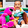 toddler, child, smiling, plush_toy, barney, bench, colorful_clothing, overalls, white_shoes, indoor, carpet, television, animation, happy, cute, playful, toy, furniture, portrait, baby