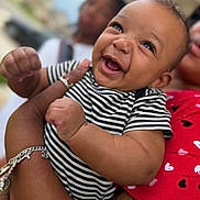 Jorel is registered to the contest to win money with this photo: baby, smiling, striped_clothing, happy, infant, person, adult, holding, red_shirt, heart_pattern, bracelet, tattoo, portrait, outdoor, blurred_background, closeup, cute, joyful, skin, face