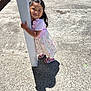 child, girl, dress, post, concrete, shadow, sunlight, outdoor, smile, sandals, car, sidewalk, flower_pattern, hair, happy, daylight, playful, person, young, curly_hair