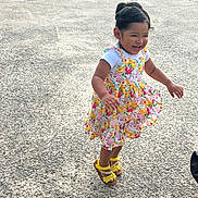 Rocio is registered to the contest to win money with this photo: child, girl, jumping, smiling, dress, floral, yellow_sandals, concrete, outdoor, happy, cute, playful, grass, sunlight, laughter, hair_tied, summer, joyful, portrait, person