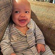 Kenzo is registered to the contest to win money with this photo: baby, smiling, striped_pajamas, couch, cozy, indoor, child, happy, infant, face, hands, seated, home, furniture, casual, light, expression, skin, clothing, portrait