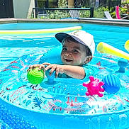 Jayden a rejoint le concours — aidez-le/la à gagner de superbes lots ! toddler, child, pool, inflatable_ring, ball, water, cap, smile, outdoor, sunny, blue, toy, play, summer, happy, person, floating, backyard, garden, swimming