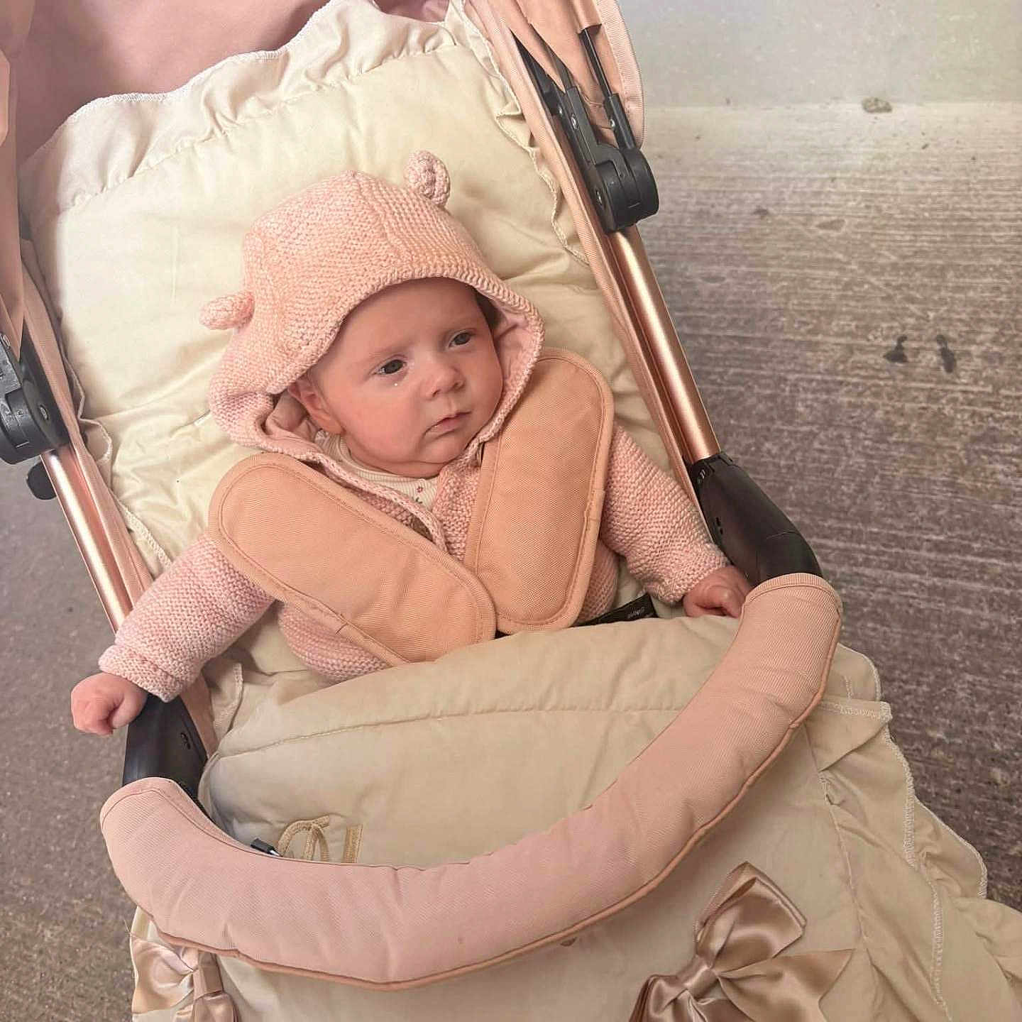 Blossom is registered to the contest to win money with this photo: baby, blanket, bow, child, cozy, curious, cute, face, infant, knit_hat, knit_sweater, outdoor, padded, person, pink, seat, small, soft_fabric, stroller, warm_clothing