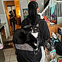 backpack, cat, cereal_box, child, clutter, countertop, doorway, fruit_bowl, hoodie, indoors, kitchen, person, ponytail, rug, staircase, staring, tile_floor, tuxedo_cat, water_bottles, wide_eyes